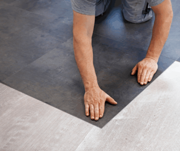 Close-up of a man laying down dark floor tiles with his hands.